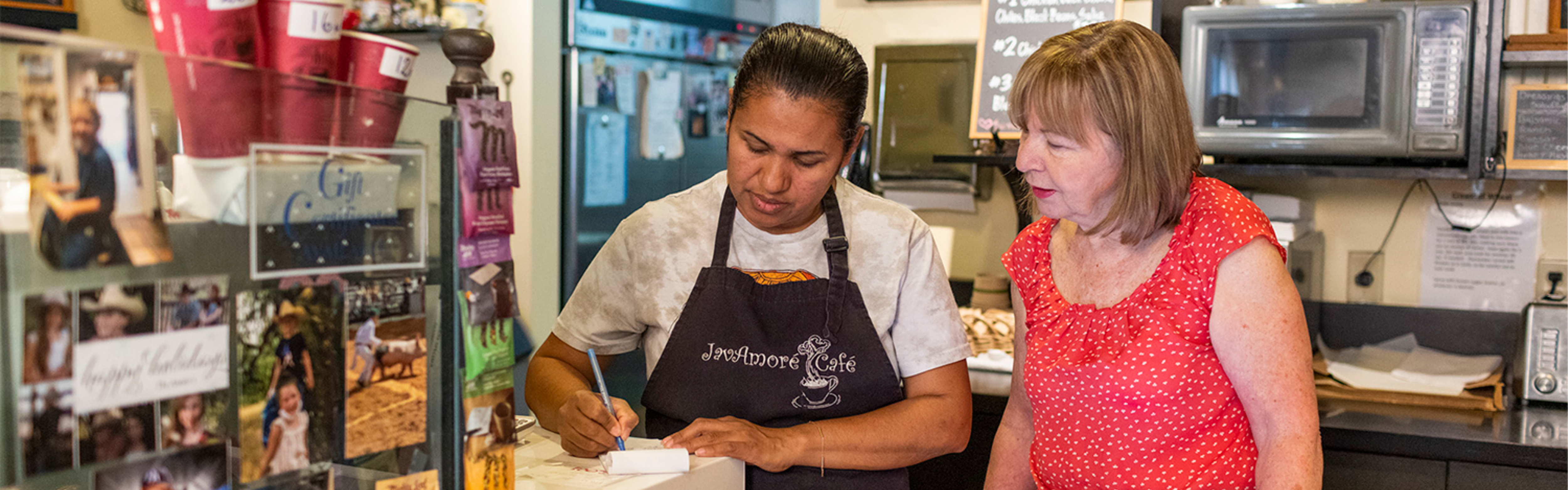 business owner and employee working together behind counter at coffee shop.