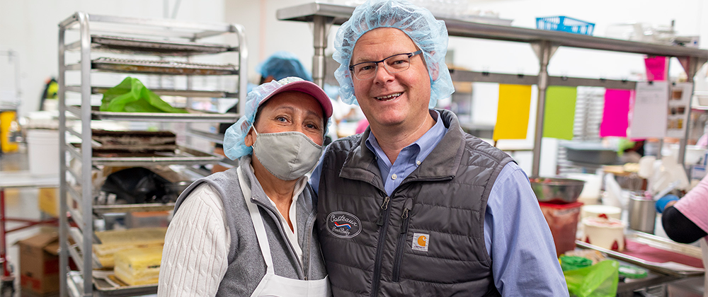 Employee and business owner posing for photo in bakery manufacturing facility.