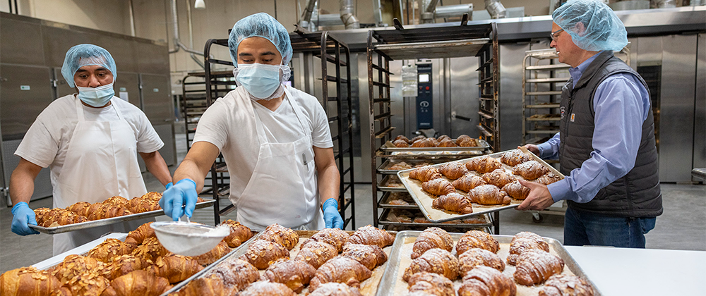 Three men preparing pastries in bakery manufacturing facility. 