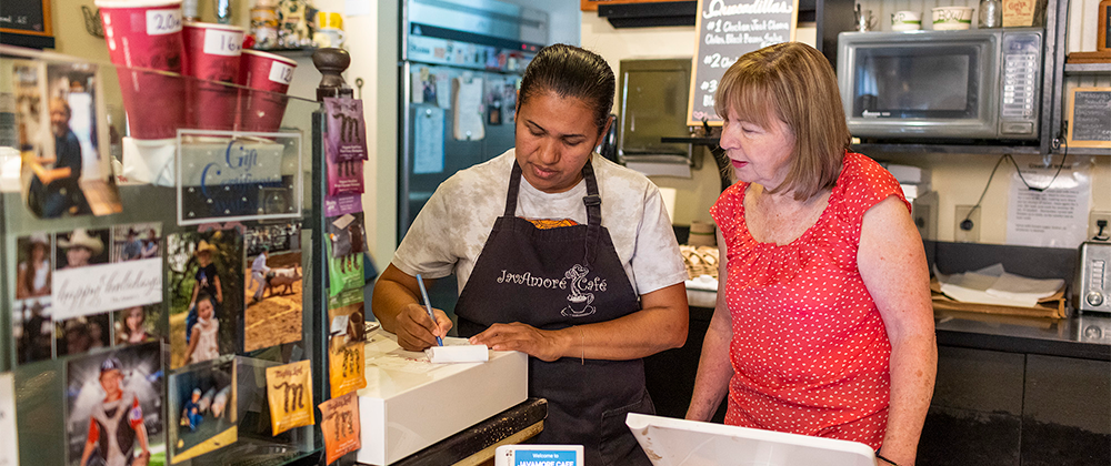 Business owner working with employee behind counter at coffee shop.